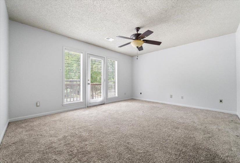 Spacious room featuring neutral carpet flooring, white walls, a ceiling fan with light fixture, and three large windows with blinds