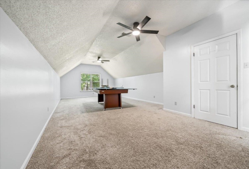 Spacious room with sloped ceilings, light-toned carpeting, and multiple ceiling fans