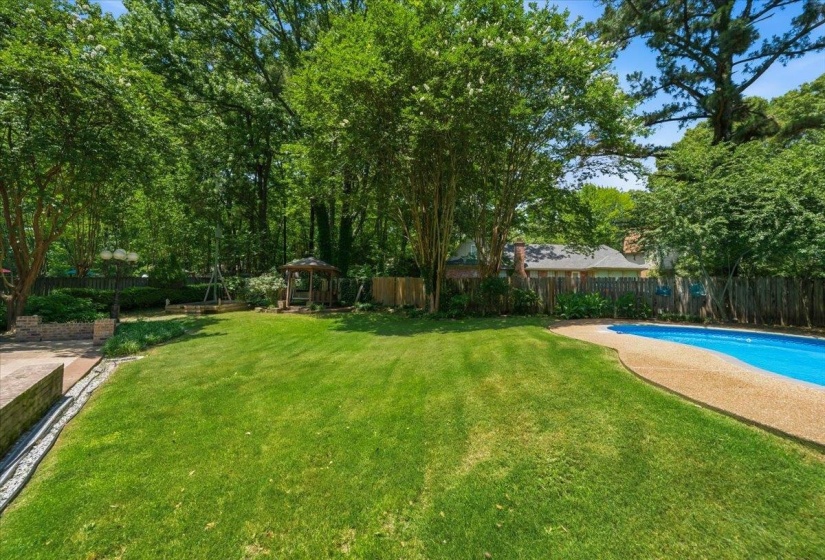 Expansive backyard featuring a lush lawn, mature trees, a swimming pool with aggregate decking, and a wooden gazebo