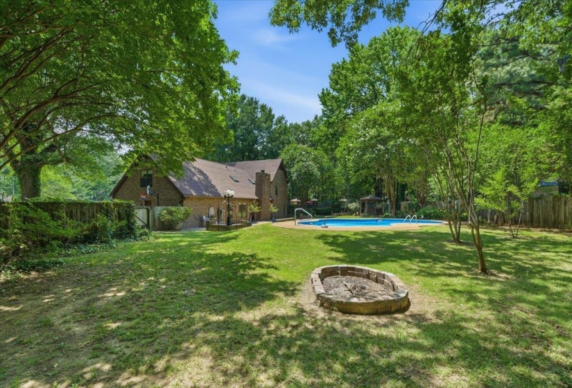 Spacious backyard featuring a swimming pool, stone fire pit, extensive lawn, and mature trees