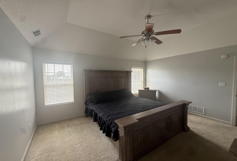 Vaulted ceiling bedroom with a ceiling fan, carpet flooring, and two windows