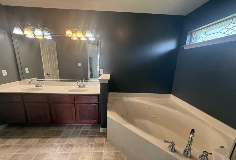 Bathroom featuring a corner jetted tub, dual vanity with undermount sinks, and a decorative transom window