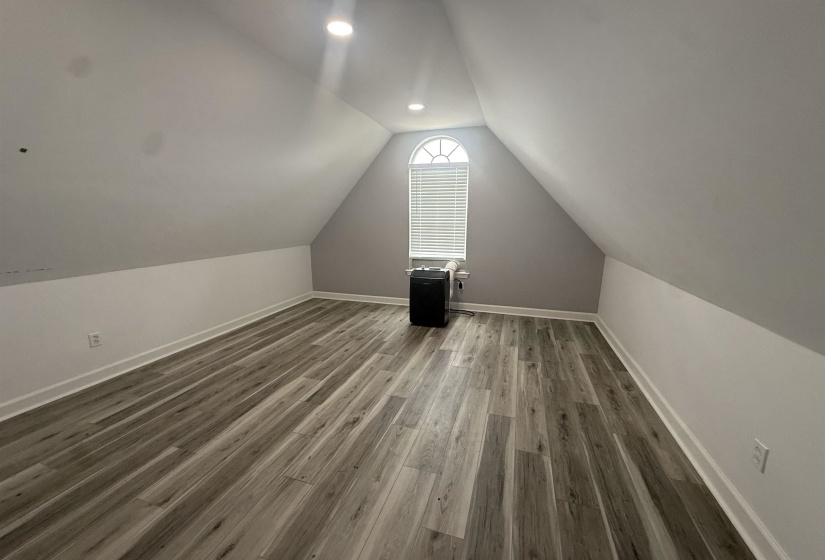 Room featuring wood-finish flooring, recessed lighting, and a window with arched transom