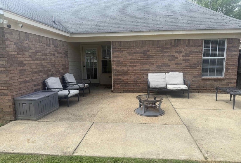 Spacious concrete patio featuring a brick exterior, double glass panel door, and a single window with blinds