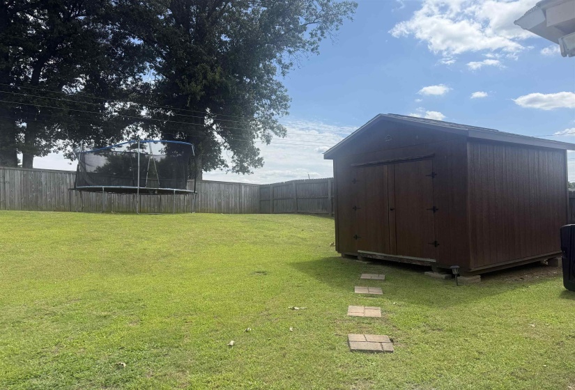 Expansive backyard featuring a manicured lawn, full privacy fencing, mature trees, and a functional storage shed with a shingled roof