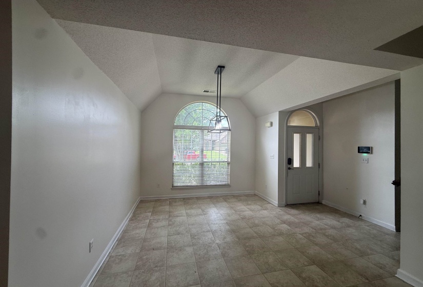Vaulted ceiling entryway featuring an arched transom window and an arched front door with frosted glass inserts, complemented by a contemporary linear pendant light fixture and neutral-toned tile flooring