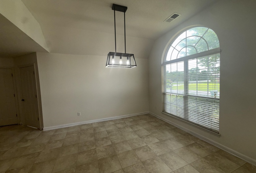 Tiled flooring throughout this space, featuring a large arched window with horizontal blinds, a modern black ceiling light fixture, and vaulted ceilings