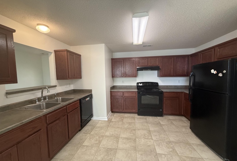 Kitchen featuring extensive dark wood-finish cabinetry, a double basin stainless steel sink, black appliances including a range, dishwasher, and refrigerator, and tiled flooring