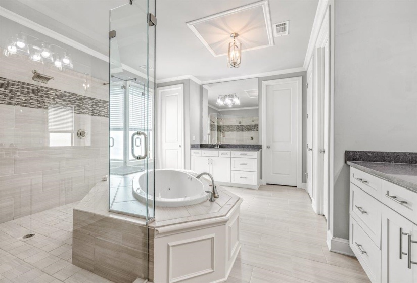 Spacious bathroom featuring a glass-enclosed shower, a built-in jetted tub, two white vanity cabinets with dark countertops, and tile flooring