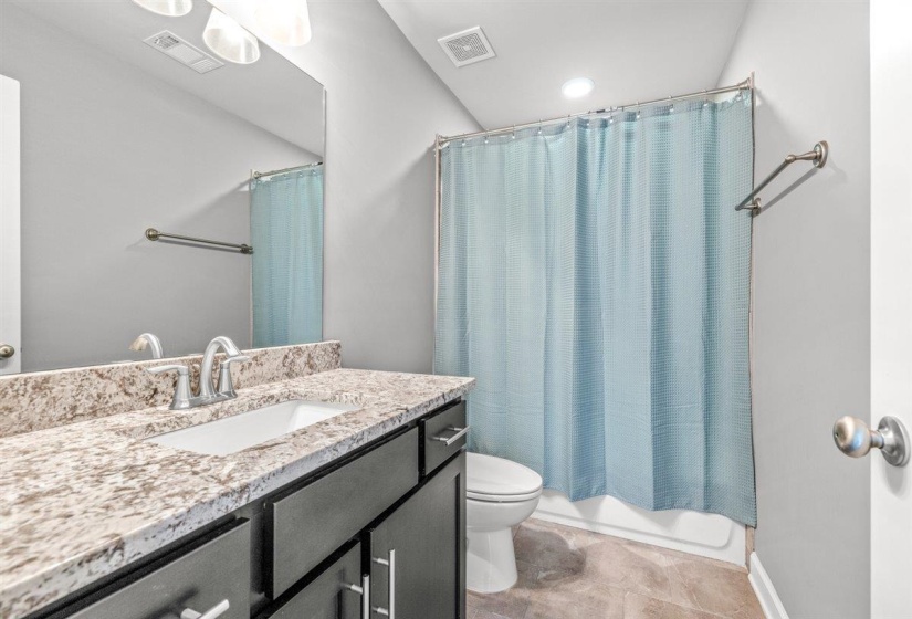 Bathroom featuring a dark wood-finish vanity with a light-toned stone countertop, integrated rectangular sink, and chrome fixtures