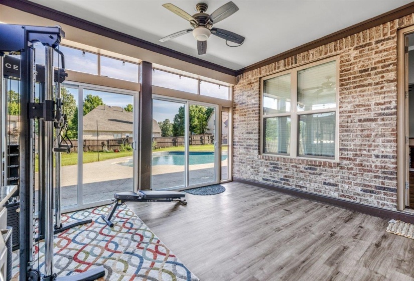 Sunroom featuring brick walls, wood-finish flooring, a ceiling fan, and extensive glass doors opening to a concrete patio and swimming pool