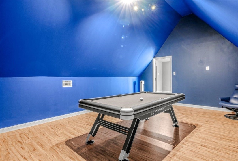 Spacious room with sloped ceilings, wood-finish flooring, recessed lighting, and a white trim baseboard