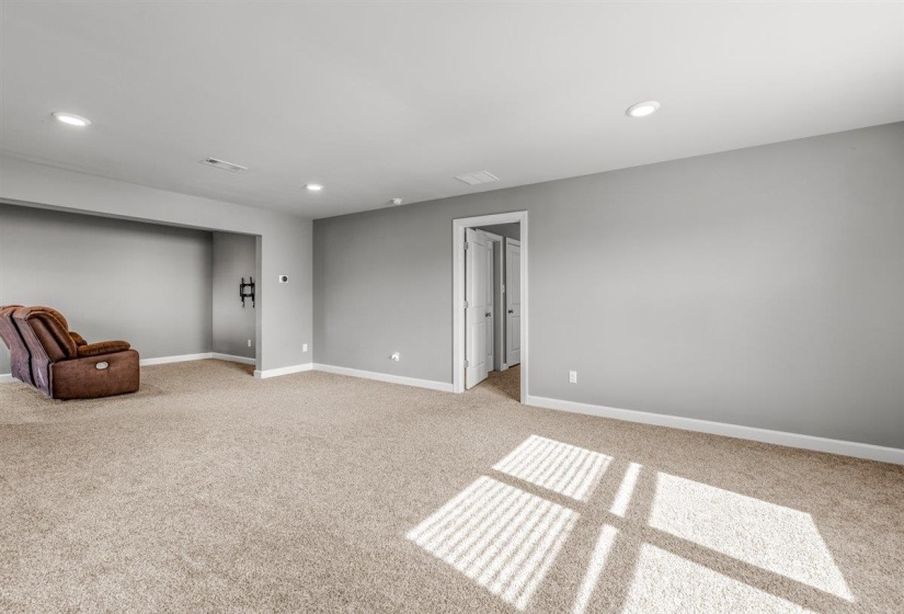 Spacious carpeted room featuring light gray walls, white trim, recessed lighting, and a doorway with double white paneled doors