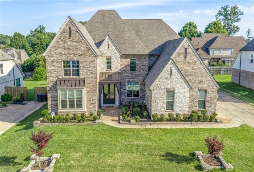 Stately two-story residence featuring a mixed brick and stone facade, a multi-gabled roofline, a covered entry, established landscaping, and a concrete driveway
