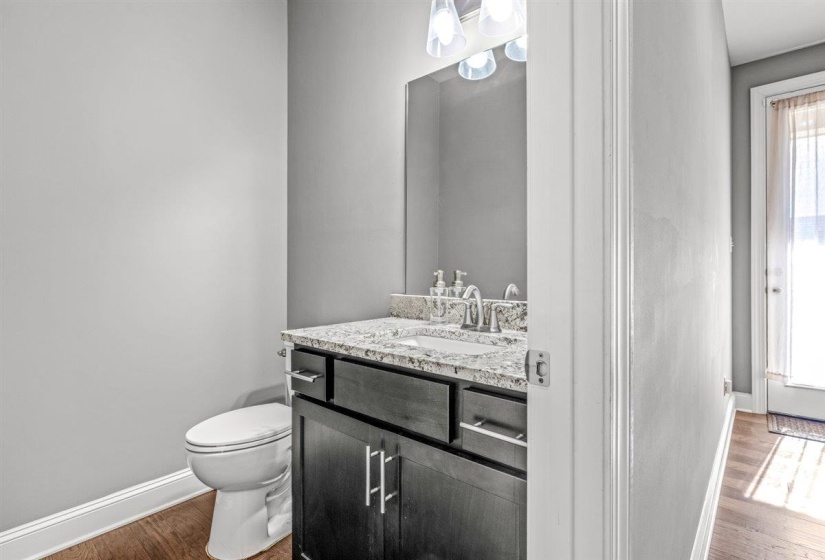 Powder room featuring a dark wood-finish vanity with a light granite countertop and undermount sink, complemented by a contemporary three-light fixture