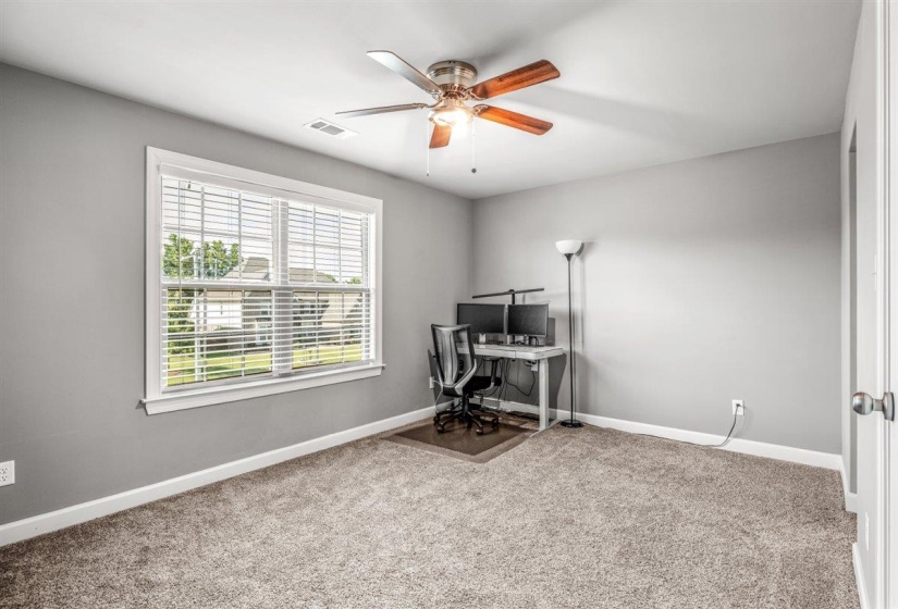 Spacious room featuring neutral carpeting, light gray wall tones, a large window with white blinds, a ceiling fan with wood-finish blades, and white trim throughout