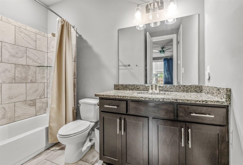 Bathroom featuring a dark wood-finish vanity with a speckled countertop, a large mirror, and a chrome-finish faucet