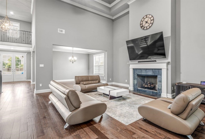 Great room featuring a fireplace with a white mantel and dark tile surround, wood-finish flooring, and a two-story ceiling with tray detailing