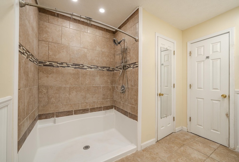 Shower enclosure featuring floor-to-ceiling tile, decorative mosaic accent band, and a built-in shower niche
