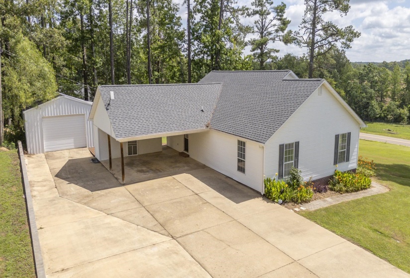 White single-story residence featuring a dark shingle roof, attached carport with support pillars, and a detached metal garage