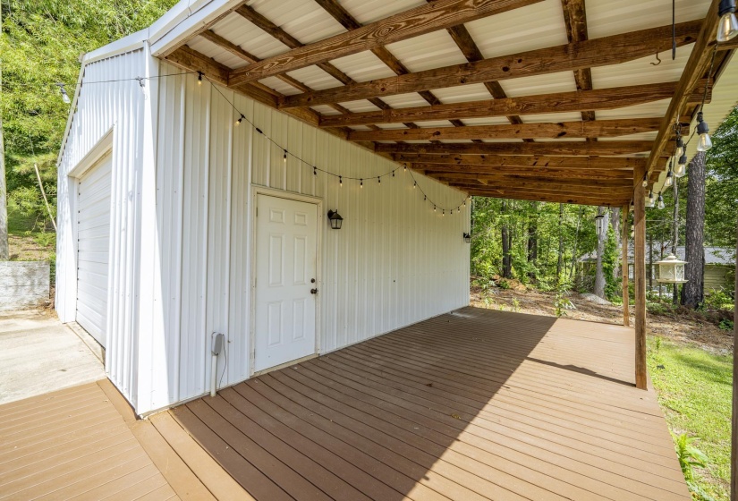 Spacious covered deck featuring a metal roof supported by exposed wood beams, a white exterior with a single entry door, and a roll-up garage door