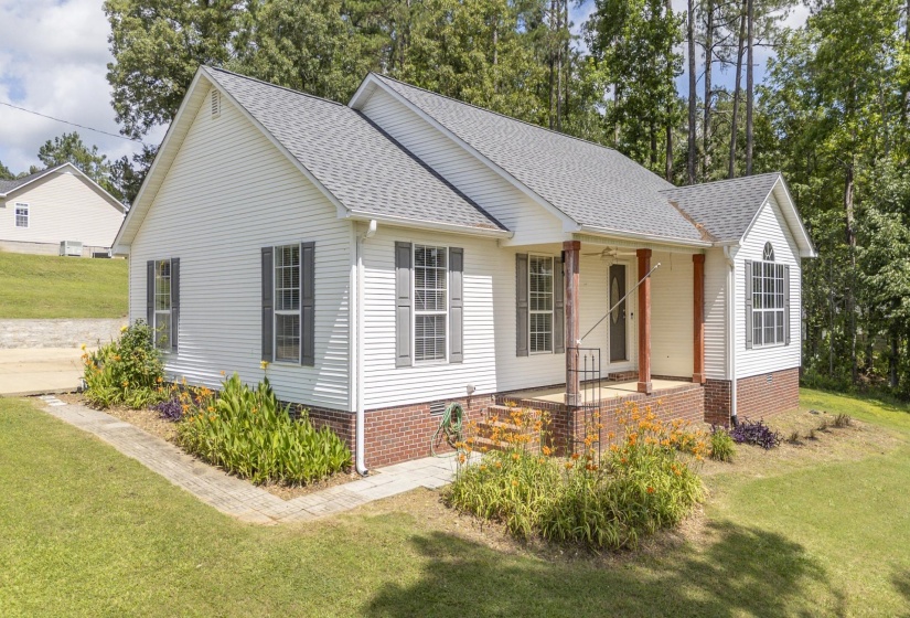 White siding exterior with a partial brick foundation, a covered front porch with wood columns, and dark shutters
