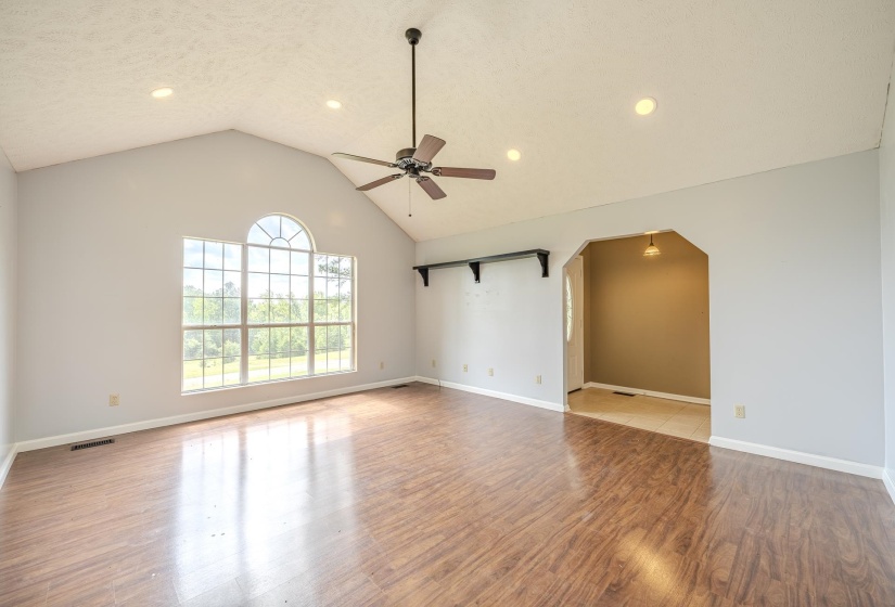 Spacious room featuring vaulted ceilings, a large arched window, wood-finish flooring, recessed lighting, and a ceiling fan