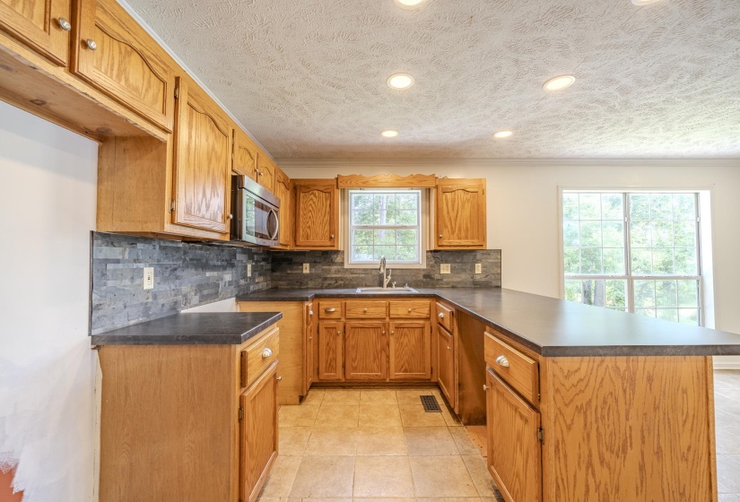 U-shaped kitchen featuring wood cabinetry, dark countertops, a stacked stone backsplash, and recessed lighting