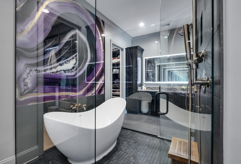 Freestanding soaking tub within a glass-enclosed wet room featuring dark mosaic tile flooring, a built-in shower system, and a striking agate-inspired wall panel
