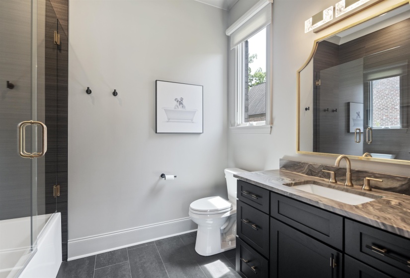Bathroom featuring a dark wood-finish vanity with a stone countertop, an undermount sink, and a gold-framed mirror