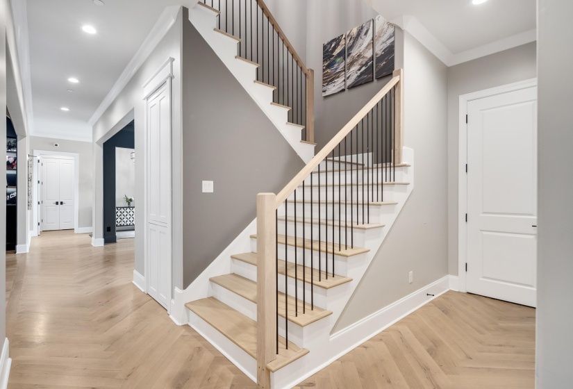 Entryway featuring a staircase with natural wood treads and black metal balusters, herringbone wood-finish flooring, recessed lighting, and white baseboards
