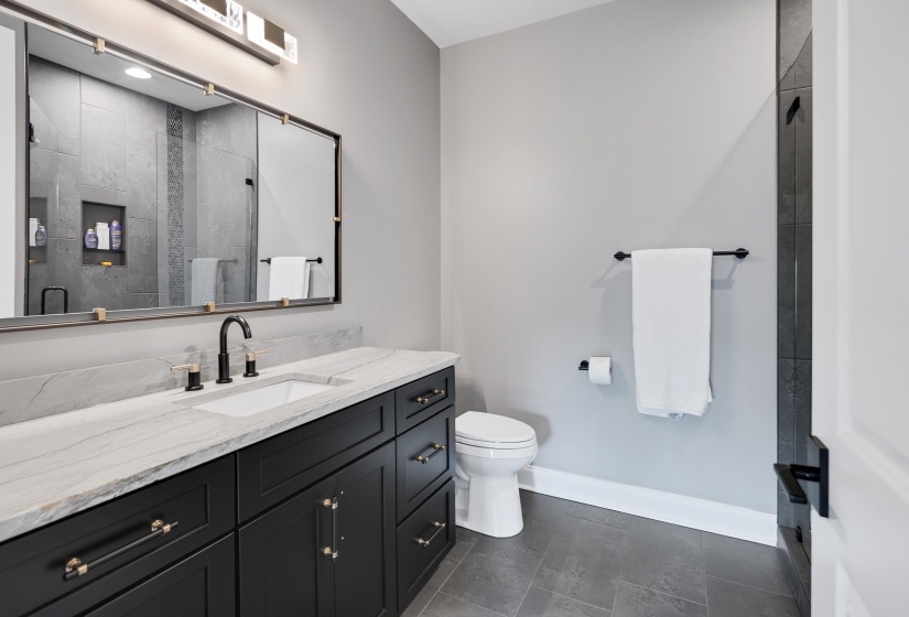 Bathroom featuring a black vanity with gold-tone hardware, white countertop with integrated sink, matte black faucet, and a large wall-mounted mirror