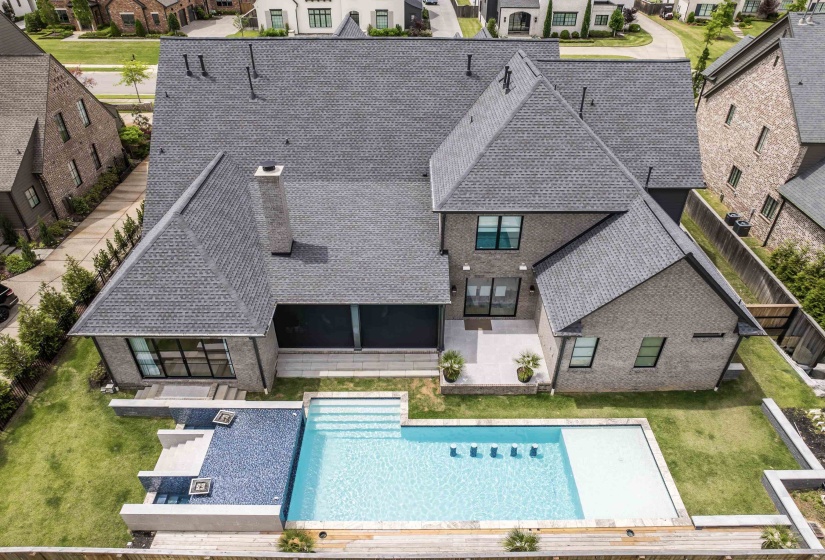 Expansive backyard featuring a rectangular swimming pool with integrated water features and a dark tiled spa