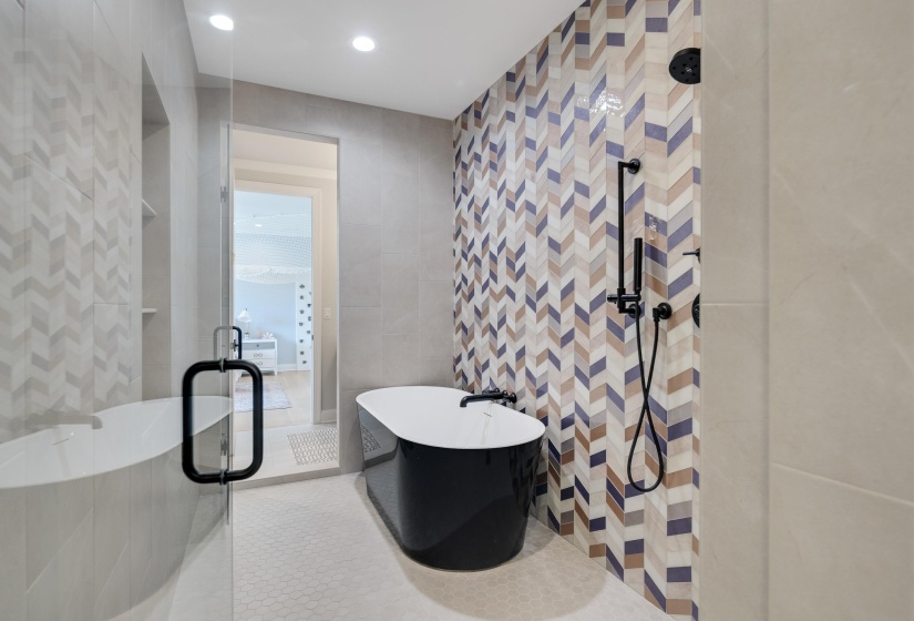 Freestanding soaking tub with a patterned chevron tile accent wall and matte black fixtures