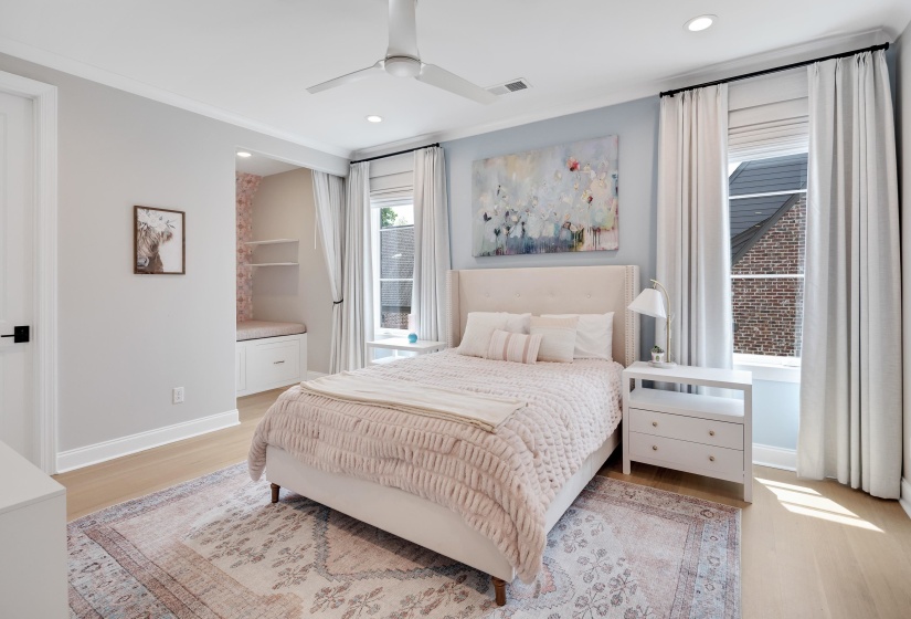 Recessed niche with built-in bench and shelving, wood-finish flooring, two large windows with full-length drapery, ceiling fan, and crown molding