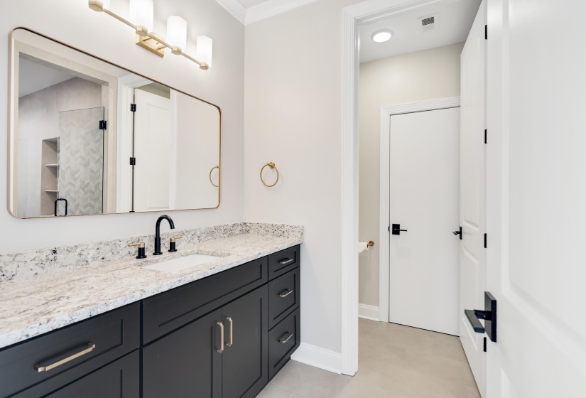 Bathroom featuring a dark wood-finish vanity with gold-tone hardware, a white countertop with grey veining, and a rectangular undermount sink with a black faucet
