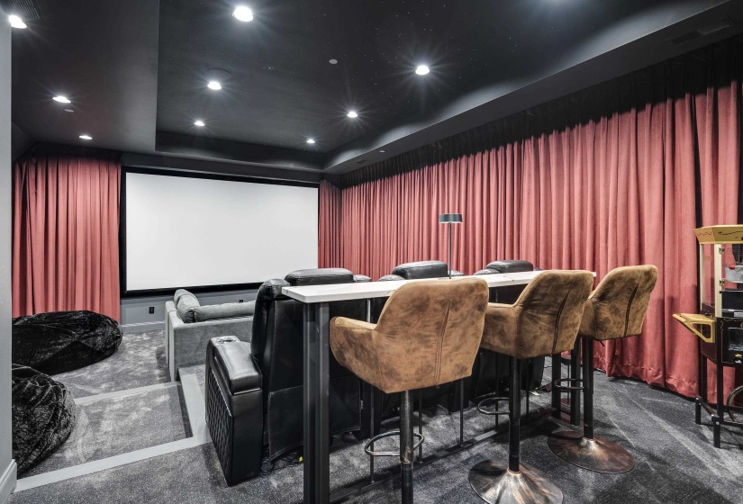 Dedicated media room featuring a large projection screen, dark ceiling with recessed lighting, and full-wall coral-toned drapery