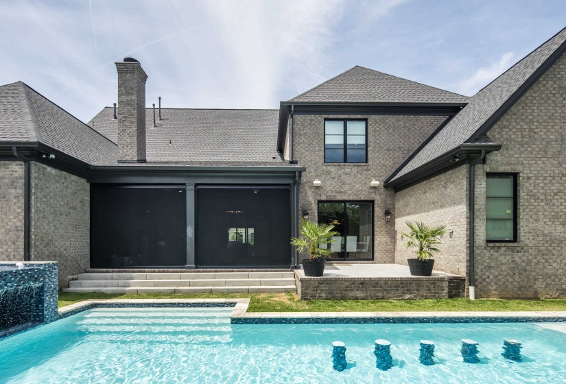 Rear exterior featuring a swimming pool with integrated seating, a brick patio, and a covered porch with privacy screens