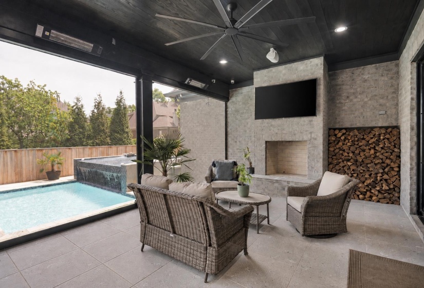 Covered outdoor living area featuring a stone fireplace, integrated television, and a wood storage alcove