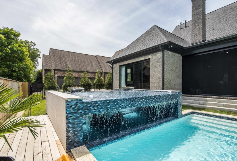 Contemporary pool featuring a glass-fronted infinity edge, blue mosaic tile accents, and a built-in step entry