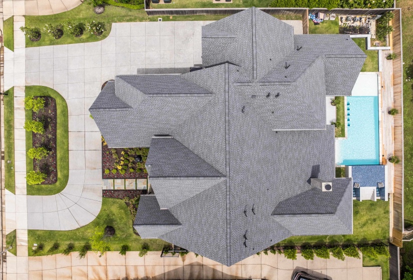 Expansive property featuring a multi-gabled roofline, concrete driveway, lush green lawns, manicured landscaping, and a rectangular swimming pool with surrounding hardscaping