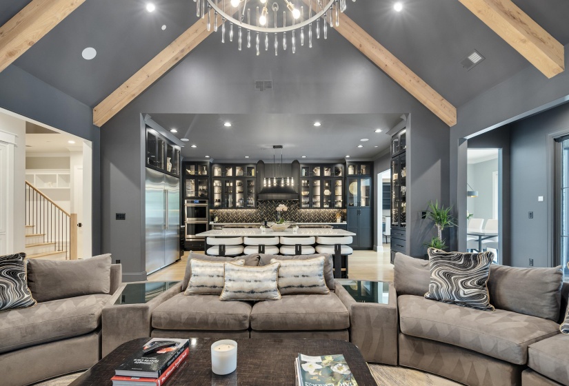 Great room featuring a vaulted ceiling with exposed wood beams, a contemporary crystal chandelier, and recessed lighting