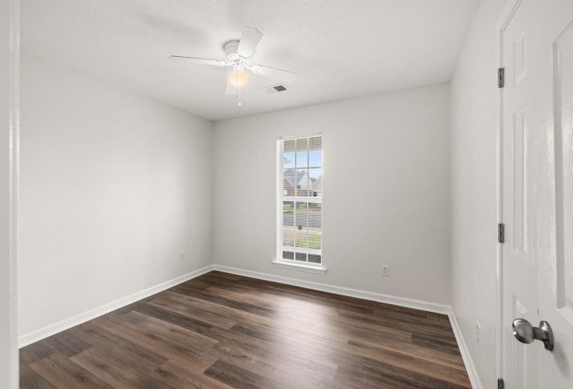 Spacious room featuring wood-finish flooring, crisp white walls, and a multi-pane window