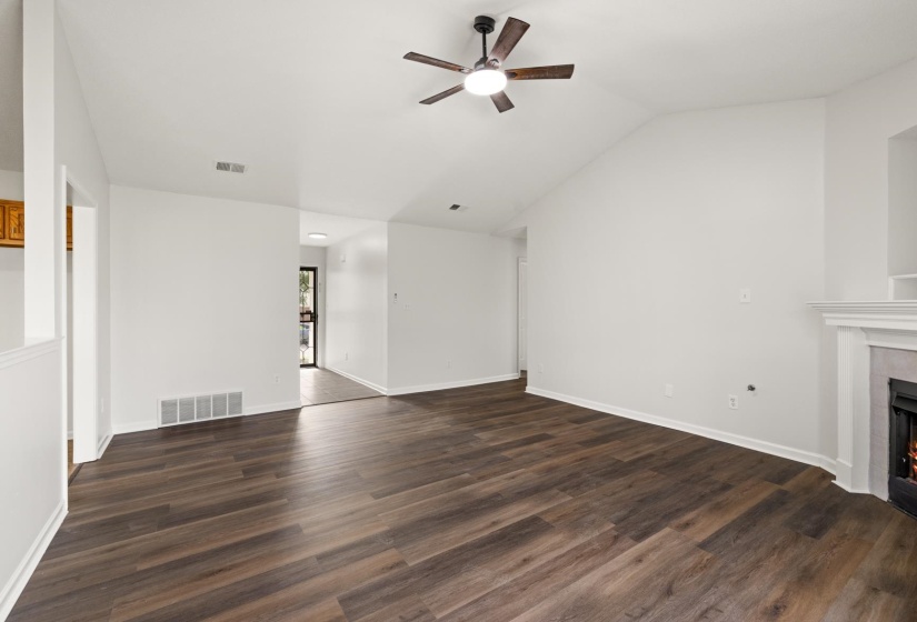 Vaulted ceiling living area featuring wood-finish flooring, a contemporary ceiling fan with integrated lighting, and a fireplace with a mantel