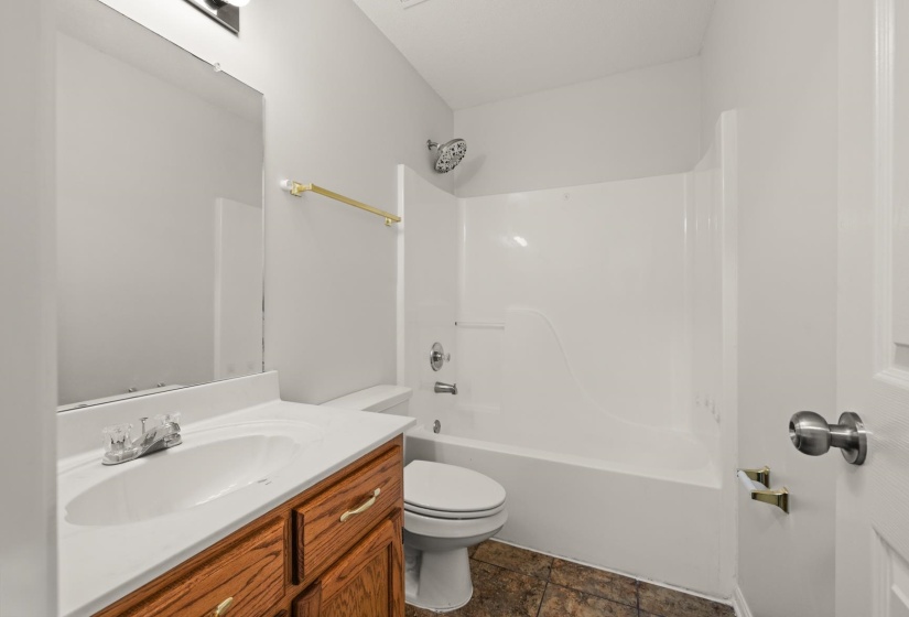 Bathroom featuring a wood-finish vanity with an integrated sink, a white countertop, and a shower-over-tub combination with a white surround