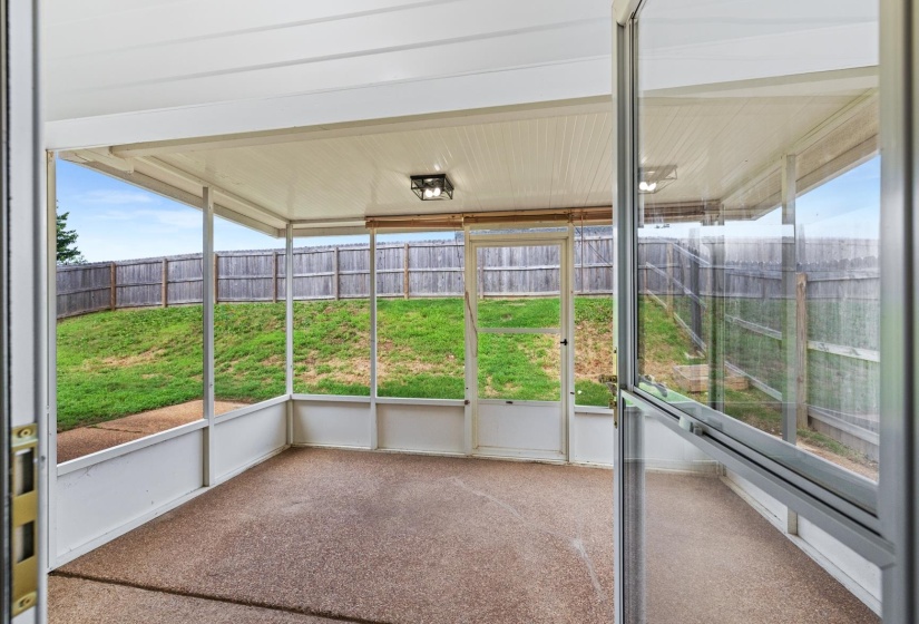 Screened porch with textured concrete flooring, white ceiling, and a modern flush-mount light fixture