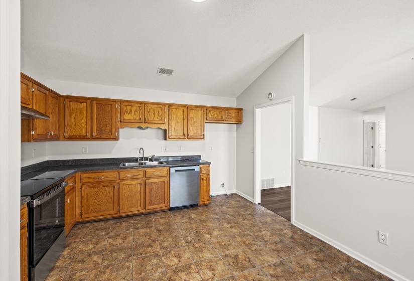 Kitchen featuring wood cabinetry, dark countertops, a stainless steel dishwasher, and a built-in electric range with an overhead vent