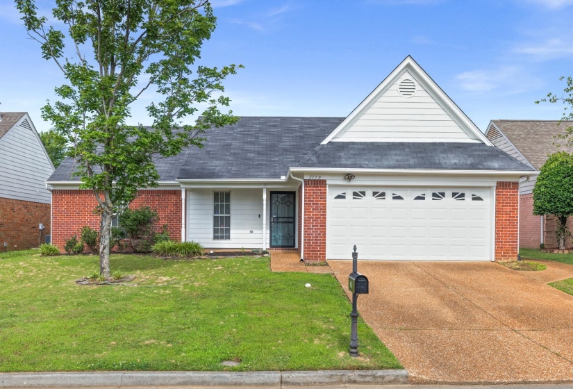 Brick and siding exterior featuring a single-car garage, mature front yard tree, covered porch entrance, and a paved driveway
