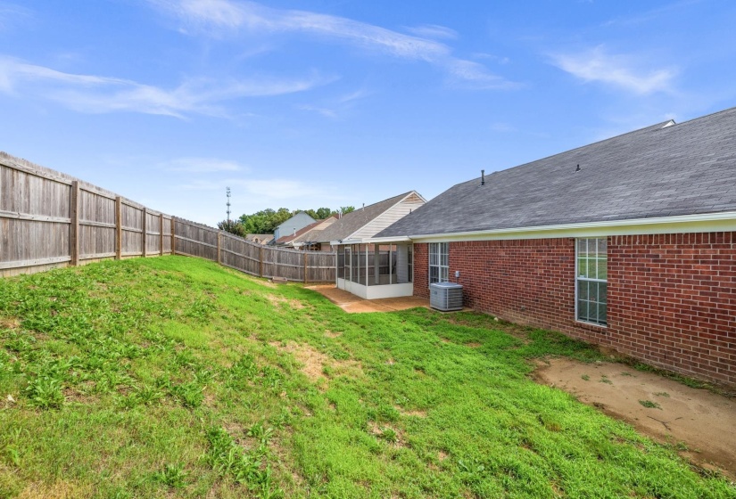 Expansive backyard featuring a partial wood fence, sloped grassy area, and a screened patio