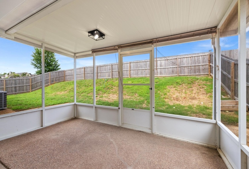 Screened-in porch featuring a textured concrete floor, white frame enclosure, and a black flush-mount ceiling light